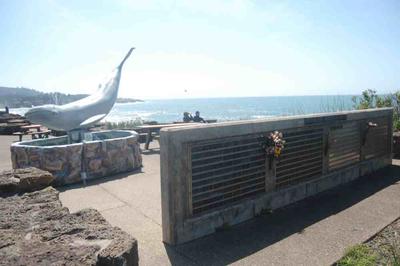 Couple in distance facing the Bay, Whale statue and short wall with bouquet of flowers in foreground